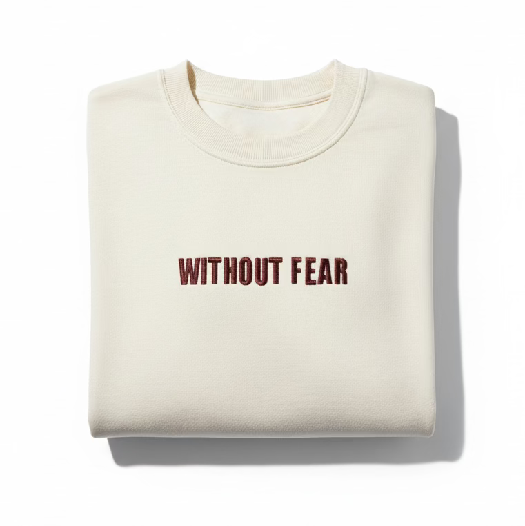 Beige t-shirt with 'WITHOUT FEAR' text on a wooden surface