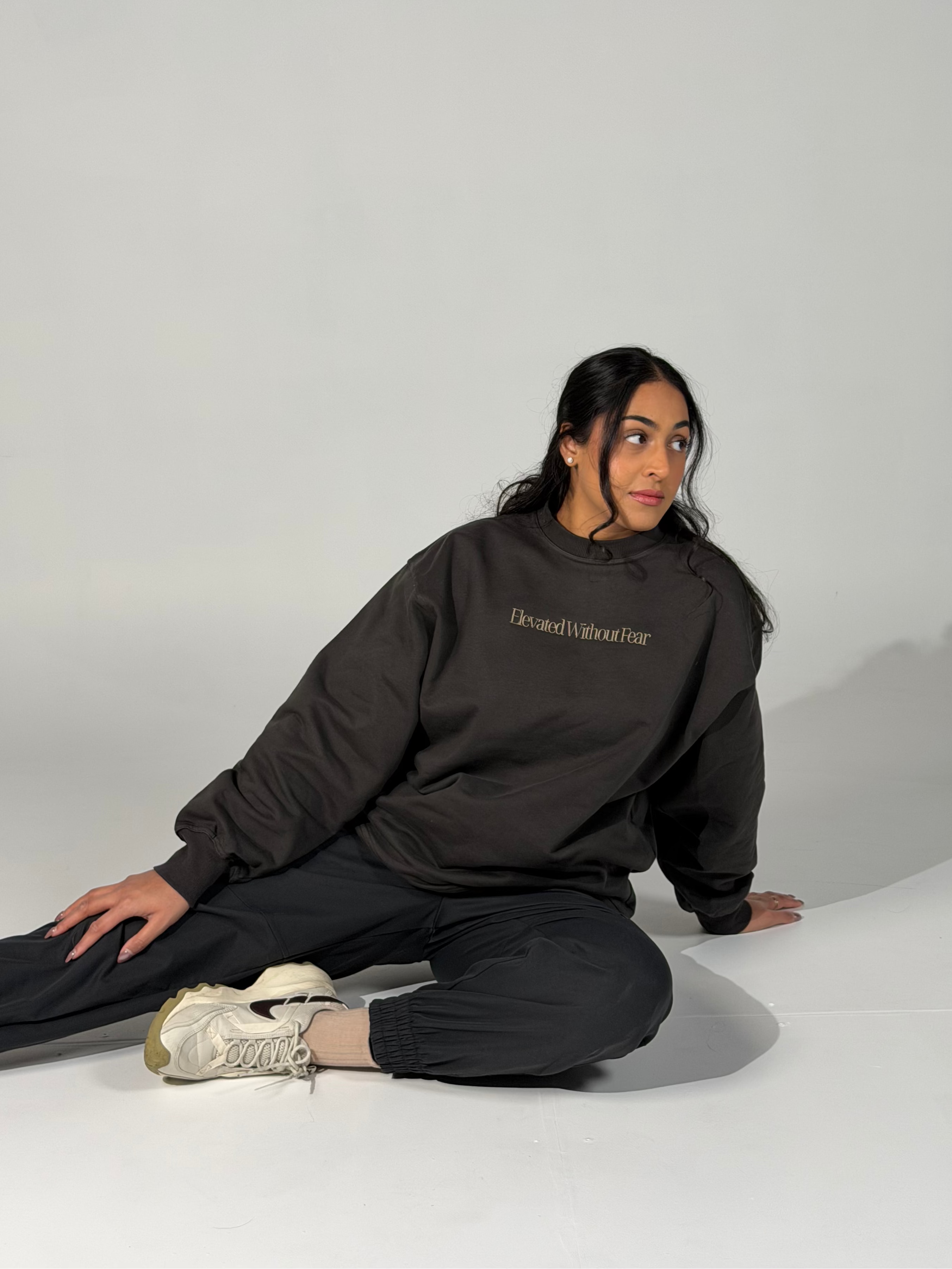 Person wearing a black sweatshirt with text, sitting on a white floor against a light gray background
