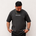 A man wearing a dark charcoal gray t-shirt with 'withoutfear' printed in white on the chest, paired with black shorts, standing against a light textured wall.